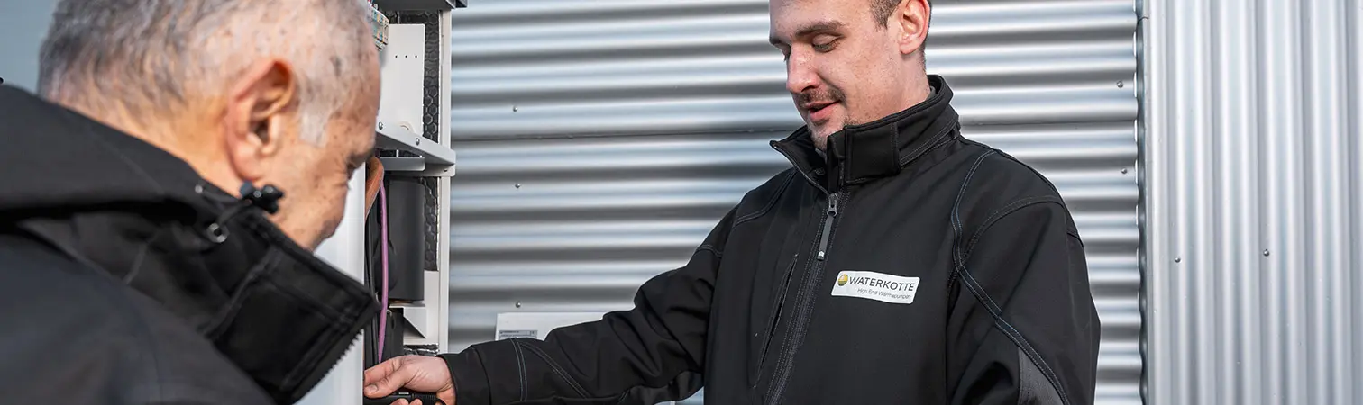 Two Waterkotte service technicians are servicing the outdoor unit of an air source heat pump.