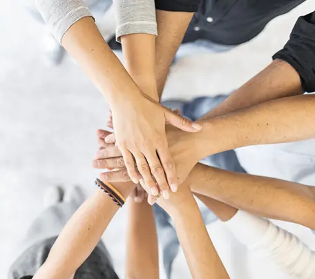 Hands placed on top of one another, symbolizing collaboration.