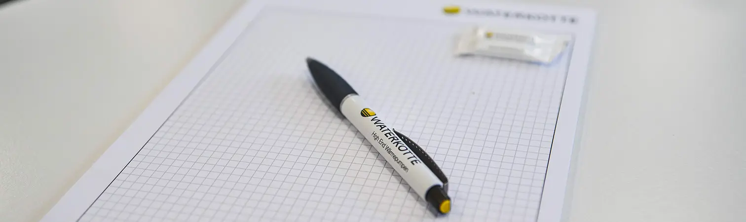 A notepad and pen featuring the Waterkotte logo are laid out on a table in the Waterkotte Academy, prepared for a training session.