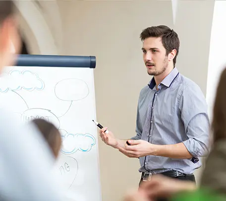 A presenter holding a pen stands beside a flip chart.