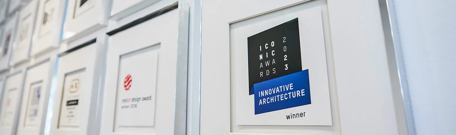 The Iconic Award for Innovative Architecture 2023 and other framed awards hang on a white wall.