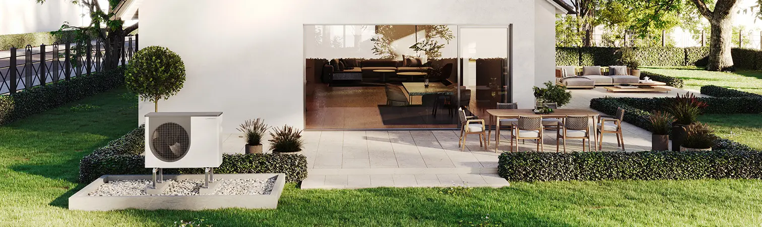 Outdoor unit of an air-source heat pump in front of a new-build home on a summer day.
