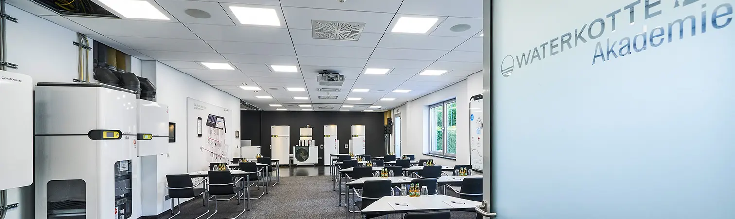 View into the training room of the Waterkotte Academy, featuring seating and a practical training area with heat pumps in the background.
