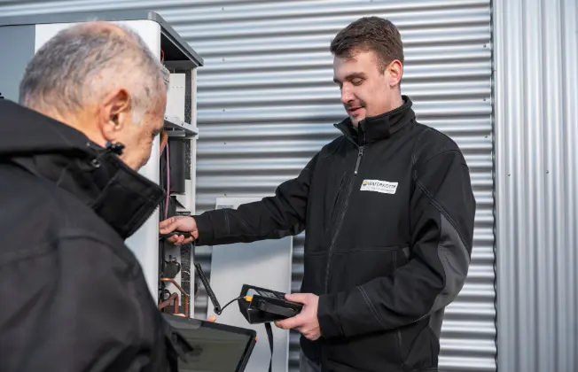 Two WATERKOTTE employees are carrying out maintenance on an outdoor air-source heat pump.