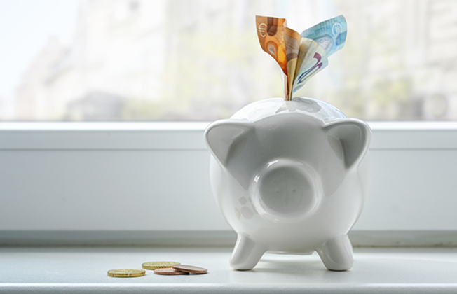 Sparschwein mit Scheinen und Münzen steht auf einer Fensterbank.