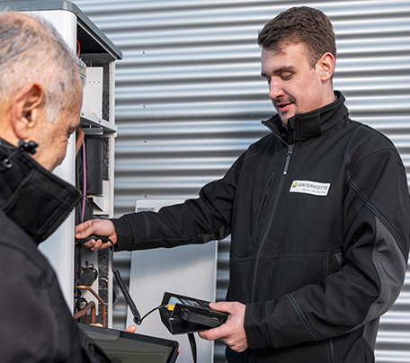 A Waterkotte service technician commissioning a Waterkotte air-source heat pump at the outdoor unit.