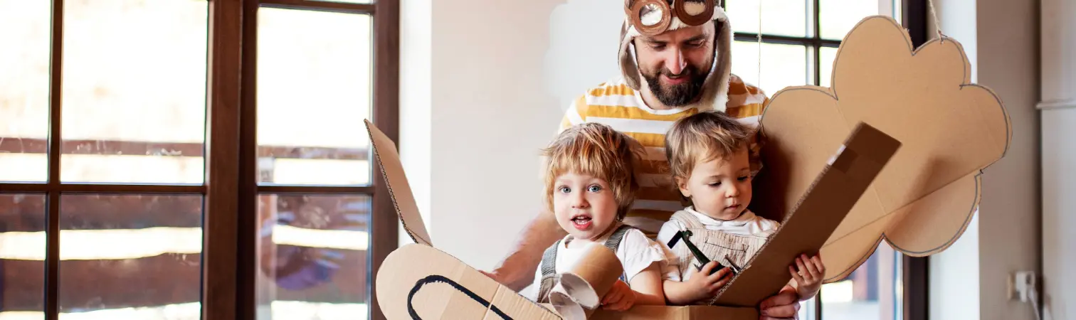 Father plays with his two small children with a cardboard airplane.