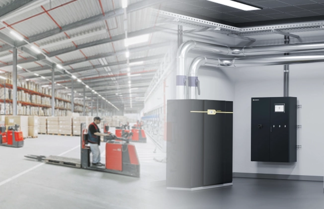 Logistikhalle mit Deckenstrahlplatten an der Decke und einer installierten Großwärmepumpe im Vordergrund; im Hintergrund arbeiten Personen im Lagerbereich.