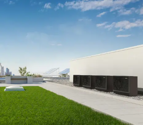Four dark gray air source heat pump outdoor units in cascade on the green roof of a modern building.