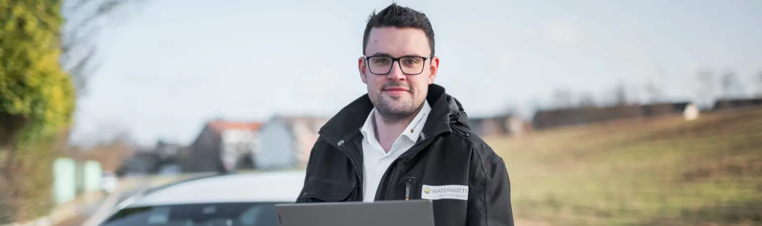Sales representative with laptop in hand in front of car.