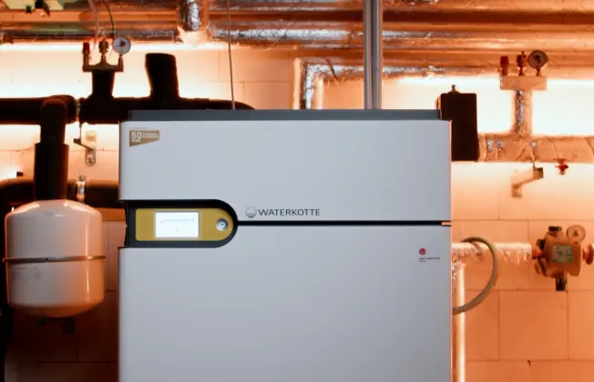 Close-up detail of the WATERKOTTE heat pump with control unit in the plant room.