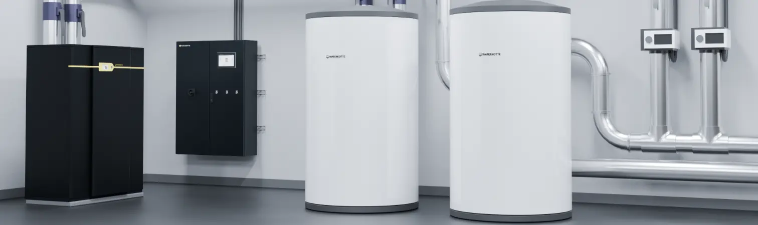 Industrial heat pump in dark gray, along with control cabinet and buffer storage tanks in large basement room in front of piping.